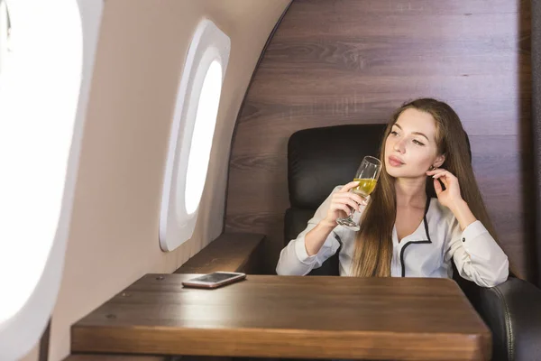 Young attractive female businessman in a private jet is drinking champagne from a glass while sitting in a chair. Service and flight first class