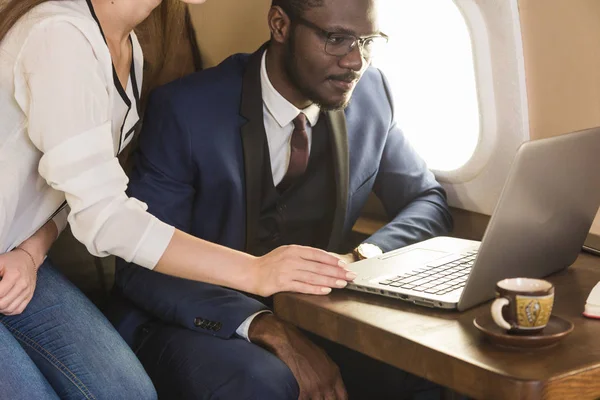 Joven empresario afroamericano exitoso con gafas y una atractiva compañera rubia en un jet privado. Servicio y vuelo de primera clase — Foto de Stock
