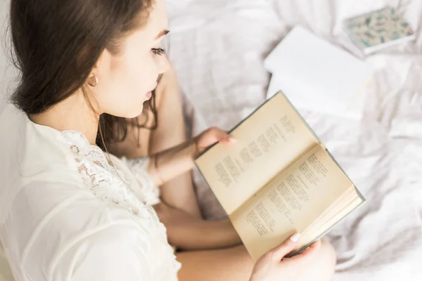 Atrakcyjna młoda dziewczyna w nocnej siedzi w łóżku i czyta książkę — Zdjęcie stockowe