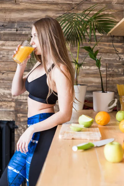 穿着运动服的迷人女孩在厨房锻炼前准备一份健康的早餐，切水果和喝果汁。健康饮食、健康和美丽的好处 — 图库照片