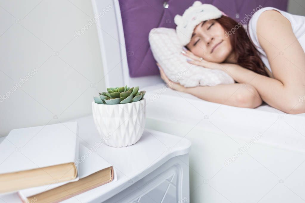 An attractive young brunette girl with brown hair sleeps in her bed in a sleep mask