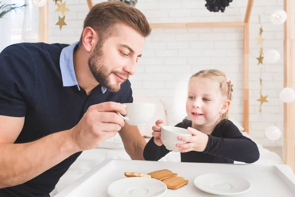 Linda niña y su padre beben té con galletas en casa . — Foto de Stock