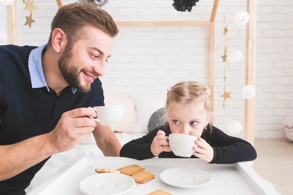 Linda niña y su padre beben té con galletas en casa . — Foto de Stock