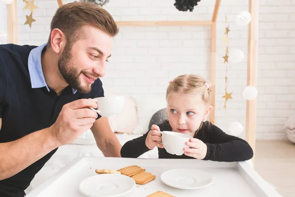 Linda niña y su padre beben té con galletas en casa . — Foto de Stock