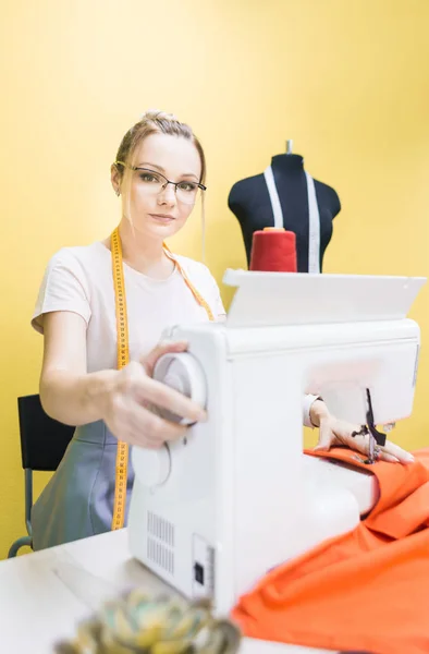 Šicí dílna. Švadlena v práci. Mladá žena, pracující s šicí stroj na barevném pozadí — Stock fotografie