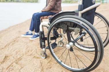 Genç bir adam onun tekerlekli sandalye yanında gölün, bir bankta oturur.