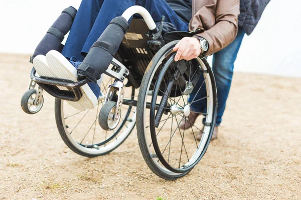 Ung man i rullstol med sin assistent på en promenad genom parken. — Stockfoto