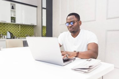 Modern bir iç mutfakta bir dizüstü bilgisayar üzerinde çalışan genç Afrikalı-Amerikalı işadamı.