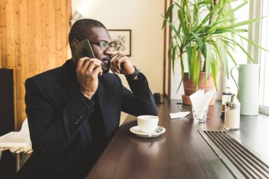 Bir kafede bir çay ile bir cep telefonu konuşurken genç yakışıklı koyu tenli işadamı.