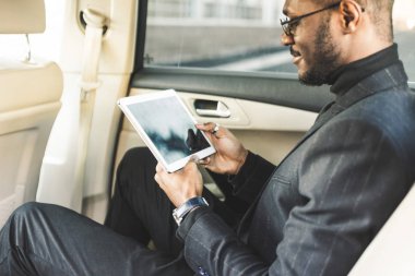 Bir arabanın arka koltukta otururken tablet kullanan genç işadamı.