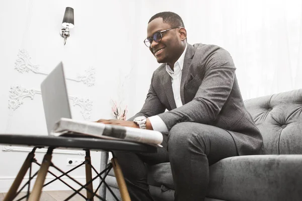 Young African American businessman in a gray suit working behind a laptop. — Stock Photo, Image