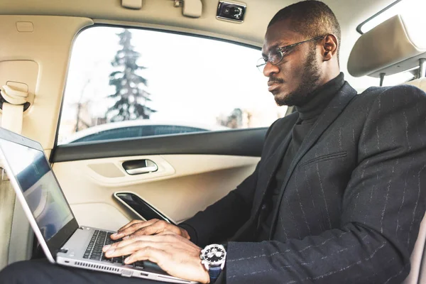 Człowiek w kombinezon biznesowy pisać na laptopie w salonie drogiego samochodu ze skórzanym wnętrzem. — Zdjęcie stockowe