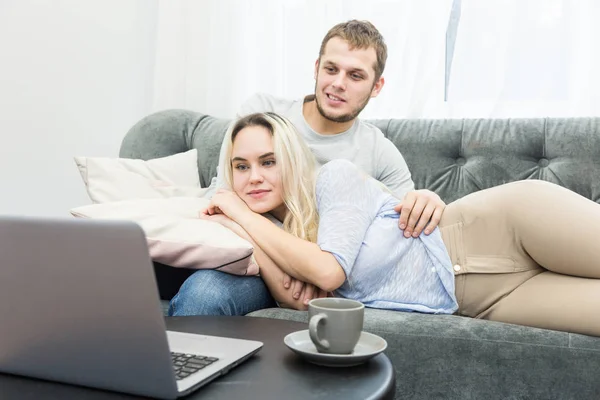 Jovem casal bonito descansando no sofá e assistindo vídeo on-line de um laptop na sala de estar . — Fotografia de Stock