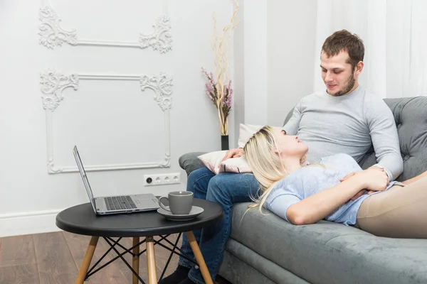 Joven hermosa pareja descansando en el sofá y viendo vídeo en línea desde un ordenador portátil en la sala de estar . — Foto de Stock