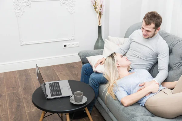 Joven hermosa pareja descansando en el sofá y viendo vídeo en línea desde un ordenador portátil en la sala de estar . — Foto de Stock