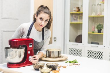Genç kadın pudra kırmızı bir elektrikli karıştırıcı metal bir kapta krem kamçı. Kavramı, ev yapımı pasta, yemek.