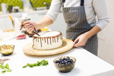 Bir şekerlemeler ahşap bir stand üzerinde beyaz krem bisküvi kek üzerine bir pasta torbası sıvı çikolata sıkır. Ev yapımı pasta kavramı, yemek pastaları.