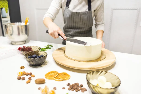 De banketbakker maakt witte room glad op een biscuittaart met een kookspatel. Het concept van zelfgemaakt gebak, het bakken van taarten. — Stockfoto