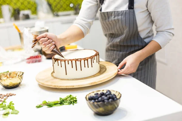 Bir şekerlemeler ahşap bir stand üzerinde beyaz krem bisküvi kek üzerine bir pasta torbası sıvı çikolata sıkır. Ev yapımı pasta kavramı, yemek pastaları.