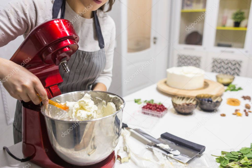 Young female confectioner whips cream in a metal bowl in a red electric mixer. The concept of homemade pastry, cooking.