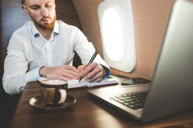 Beyaz gömlekli çekici ve başarılı bir iş adamı özel jetinin koltuğunda oturuyor..