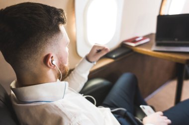 Genç ve başarılı iş adamı dinleniyor ve özel iş uçağının koltuğunda oturmuş müzik dinliyor.