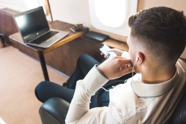 Genç ve başarılı iş adamı dinleniyor ve özel iş uçağının koltuğunda oturmuş müzik dinliyor.