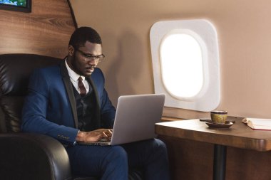 Onun özel jet sandalyede otururken gözlük bir dizüstü bilgisayar üzerinde çalışan çekici ve başarılı Afrikalı Amerikan işadamı.