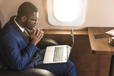 Onun özel jet sandalyede otururken gözlük bir dizüstü bilgisayar üzerinde çalışan çekici ve başarılı Afrikalı Amerikan işadamı.
