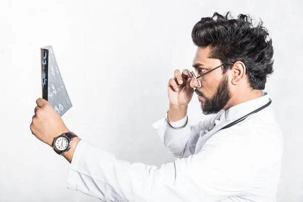 Bonito médico jovem em um casaco branco com um estetoscópio verifica atentamente o raio-x dos pacientes . — Fotografia de Stock