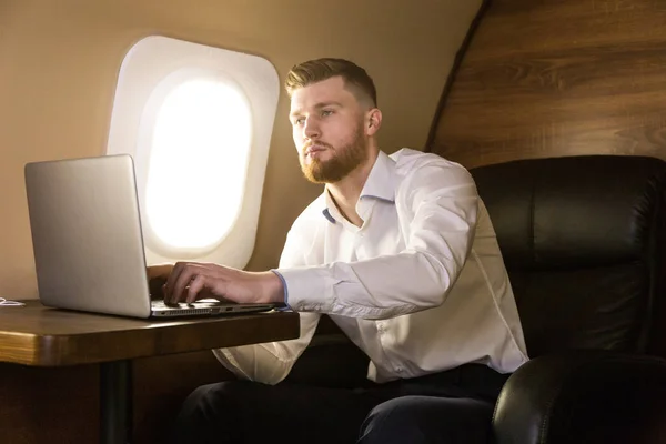 Młody, atrakcyjny i odnoszący sukcesy biznesmen pracujący w fotelu swojego prywatnego samolotu biznesowego — Zdjęcie stockowe