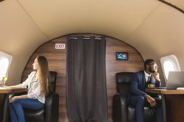 年轻成功的非洲裔美国商人戴着眼镜, 在私人飞机上金发碧眼。服务和航班头等舱 — 图库照片