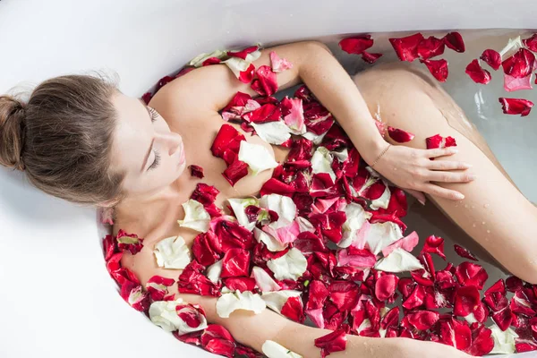 Молодая привлекательная девушка берет ванную комнату с лепестками цветов и расслабляется на фоне красивого светлого интерьера. Спа-процедуры для красоты и здоровья с уходом за кожей — стоковое фото