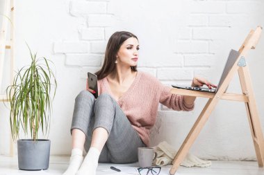 Ev yapımı günlük giysiler içinde mutlu bir kadın parlak bir iç mekanda oturur ve telefon kullanır, kız bir dizüstü bilgisayarda çalışırken ve internette sörf yaparken dinlenir. Rahat serbest çalışma alanı,