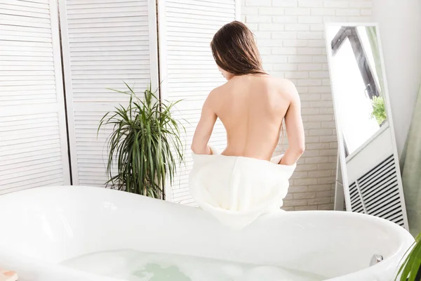 Attraente ragazza in accappatoio bianco applica la crema sulla pelle mentre si siede all'interno del bagno e facendo procedure mattutine. Cura della pelle e del corpo — Foto Stock