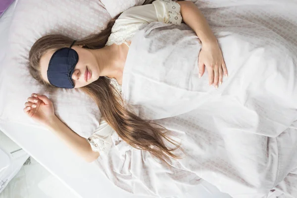 Beautiful young girl sleeping in the morning in her bed with a face mask. View from above — Stock Photo, Image