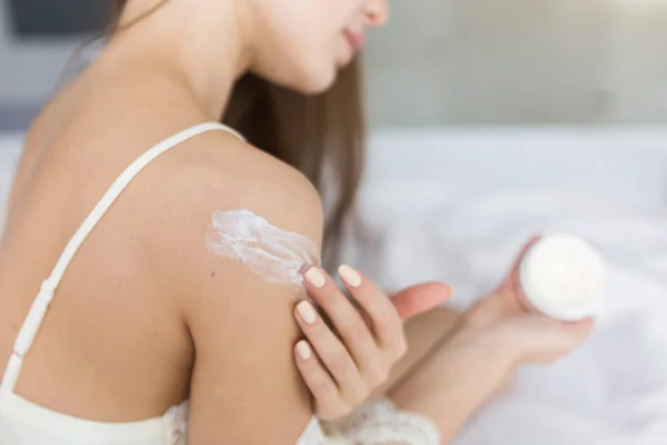 Attractive young girl in night clothes applies cream to skin and rubs it while doing morning procedures. Moisturizing and skin care