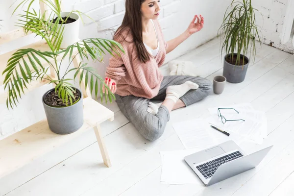 Молода щаслива жінка сидить на підлозі в позі йоги в світлій квартирі і працює за ноутбуком, дівчина-фрілансер медитує під час роботи. межа напруги . — стокове фото