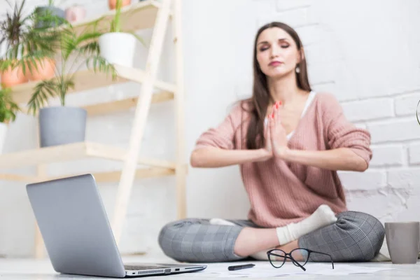 Молода щаслива жінка сидить на підлозі в позі йоги в світлій квартирі і працює за ноутбуком, дівчина-фрілансер медитує під час роботи. хвилювання та натхнення — стокове фото