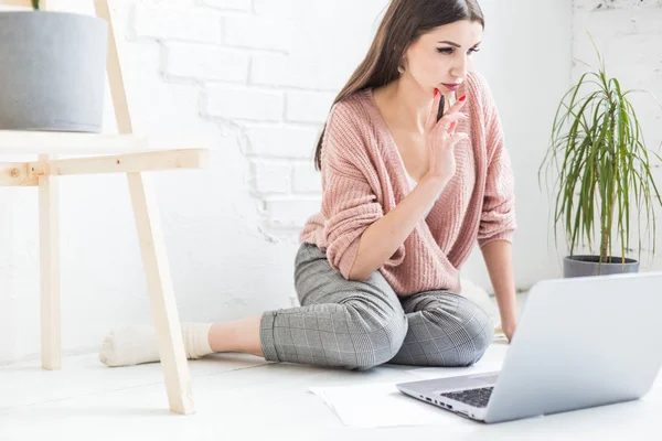 Una joven feliz mujer se sienta en el suelo en un apartamento luminoso o interior de la oficina y trabaja en un ordenador portátil, freelancer chica en el trabajo, el concepto de estudiantes de educación a distancia, papeleo y aprendizaje en línea — Foto de Stock