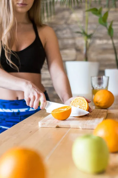 Vonzó lány a sportruházatban, aki egészséges reggelit készít a konyhában edzés előtt, gyümölcsöt vág és friss gyümölcslevet készít. Egészséges életmód, fitnesz és szépség — Stock Fotó