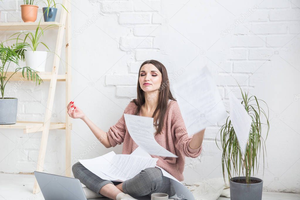 A young happy woman throws up a bunch of pieces of paper and documents sitting near the laptop, the freelance girl is happy and in a good mood. excitement and inspiration