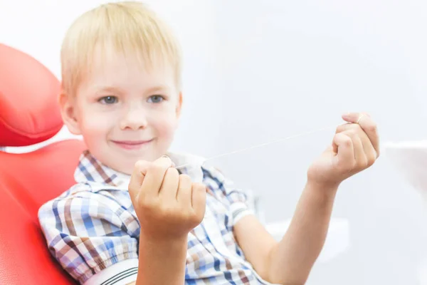 Clínica dental. Recepción, examen del paciente. Cuidado de los dientes. Un niño pequeño con hilo dental se sienta en una silla dental. Concepto de higiene oral — Foto de Stock