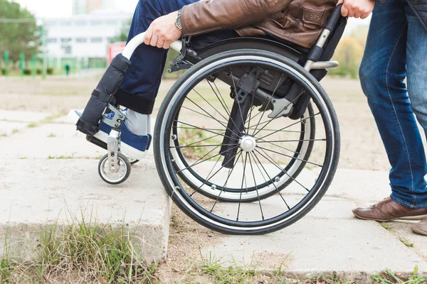 Ung man i rullstol med sin assistent på en promenad genom parken. — Stockfoto