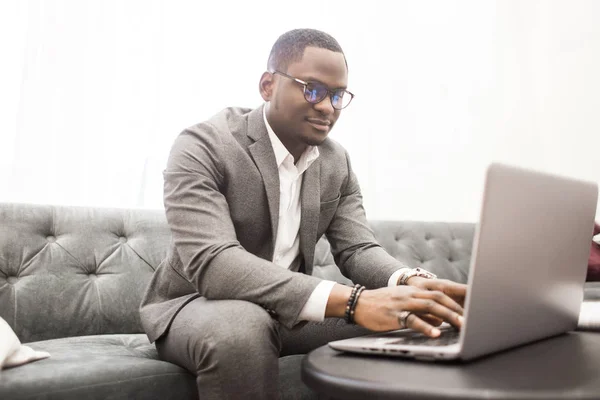 Jeune homme d'affaires afro-américain en costume gris travaillant derrière un ordinateur portable . — Photo