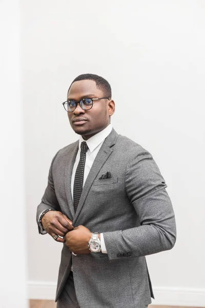 Joven hombre de negocios afroamericano en un traje gris atando una corbata sobre un fondo blanco . — Foto de Stock