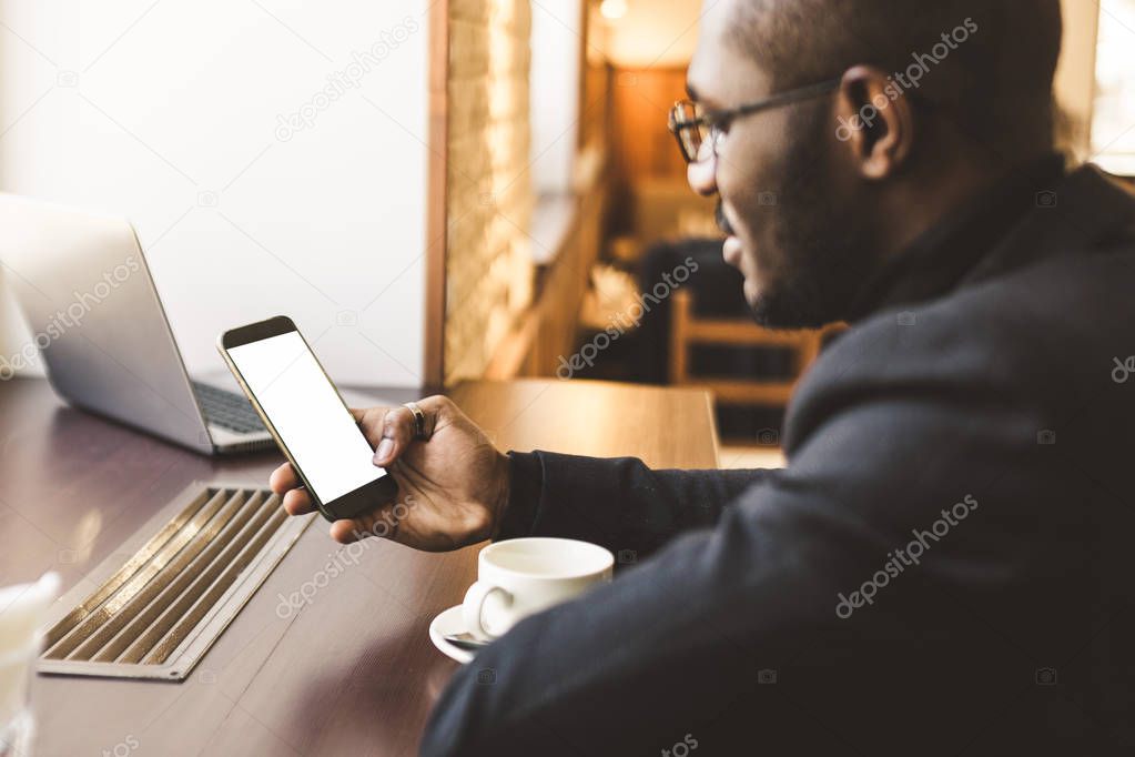 Young handsome dark-skinned businessman in a cafe talking on a cell phone with a cup of tea.