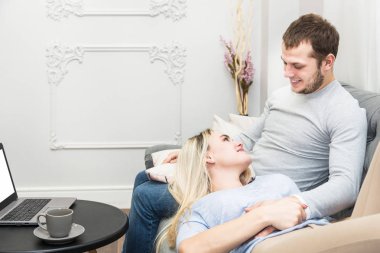 Genç güzel çift kanepede istirahat ve oturma odasında bir laptop online video izlerken.