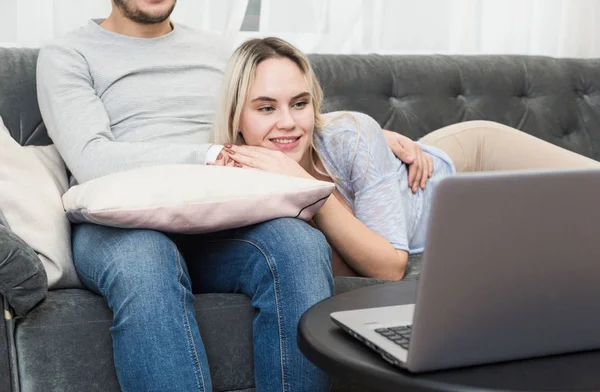 Jovem casal bonito descansando no sofá e assistindo vídeo on-line de um laptop na sala de estar . — Fotografia de Stock