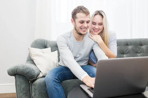 Joven hermosa pareja descansando en el sofá y viendo vídeo en línea desde un ordenador portátil en la sala de estar . —  Fotos de Stock